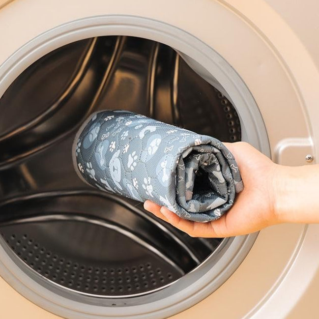 Person holding a washable dog potty pad folded fabric in front of an open washing machine with text about fabric durability.